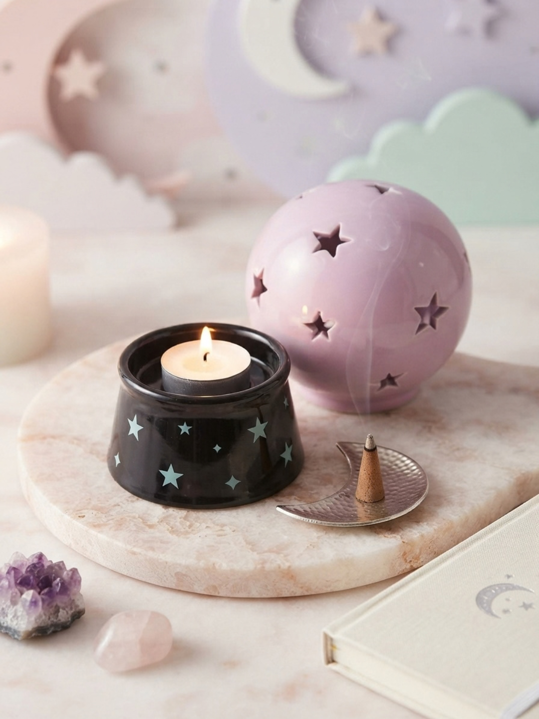 A styled tabletop scene with a pastel lavender crystal ball tea light holder and incense burner  open holding a lit tealight candle,  a small metal tray with a burning incense stick, and soft pastel decor in the background.